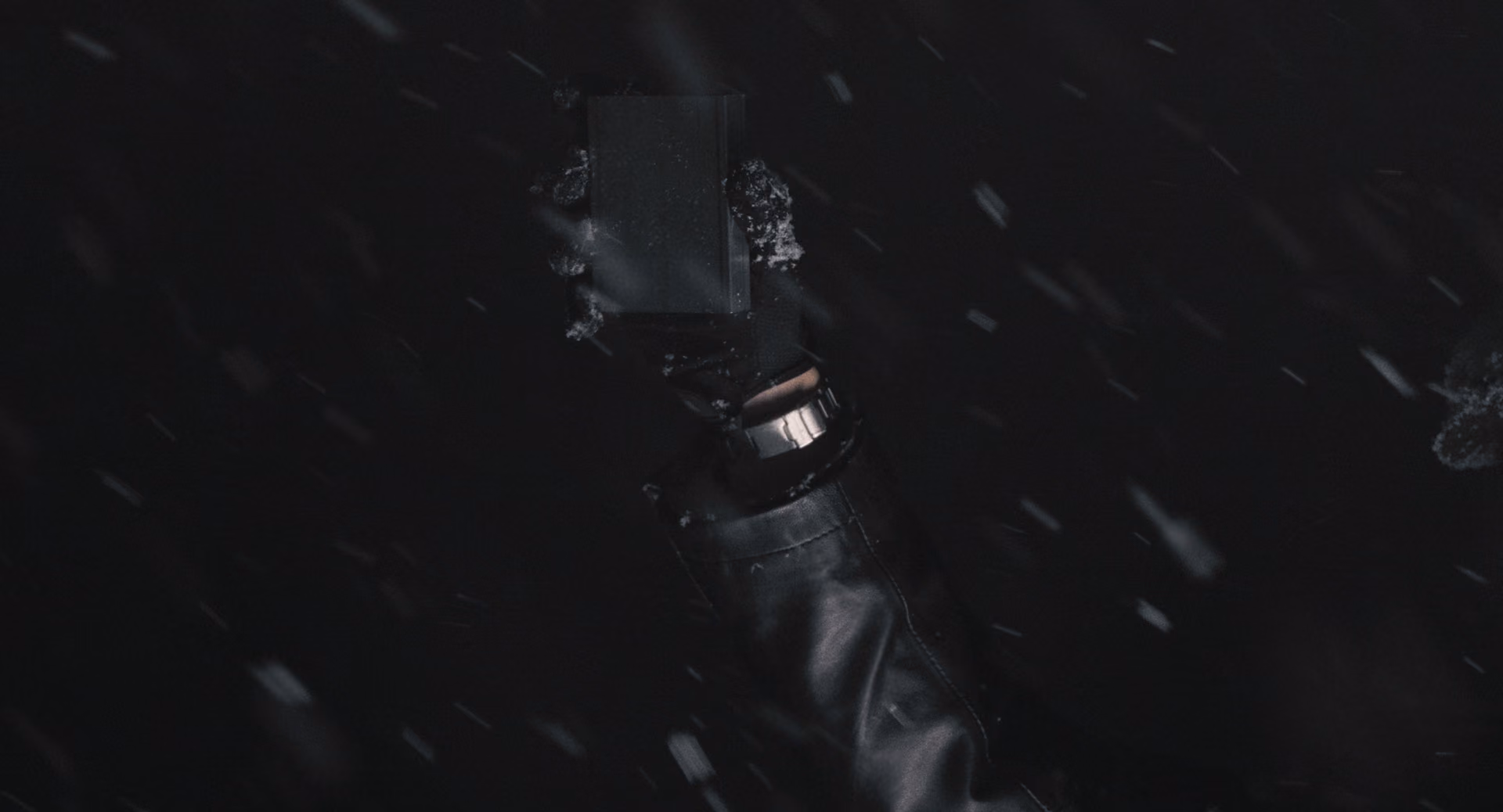 A gloved hand grips a dark handle amid pale flecks.